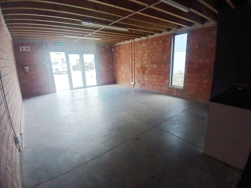 An open-plan office space featuring exposed brick walls, concrete flooring, and exposed timber ceiling joists, offering a modern industrial aesthetic.
