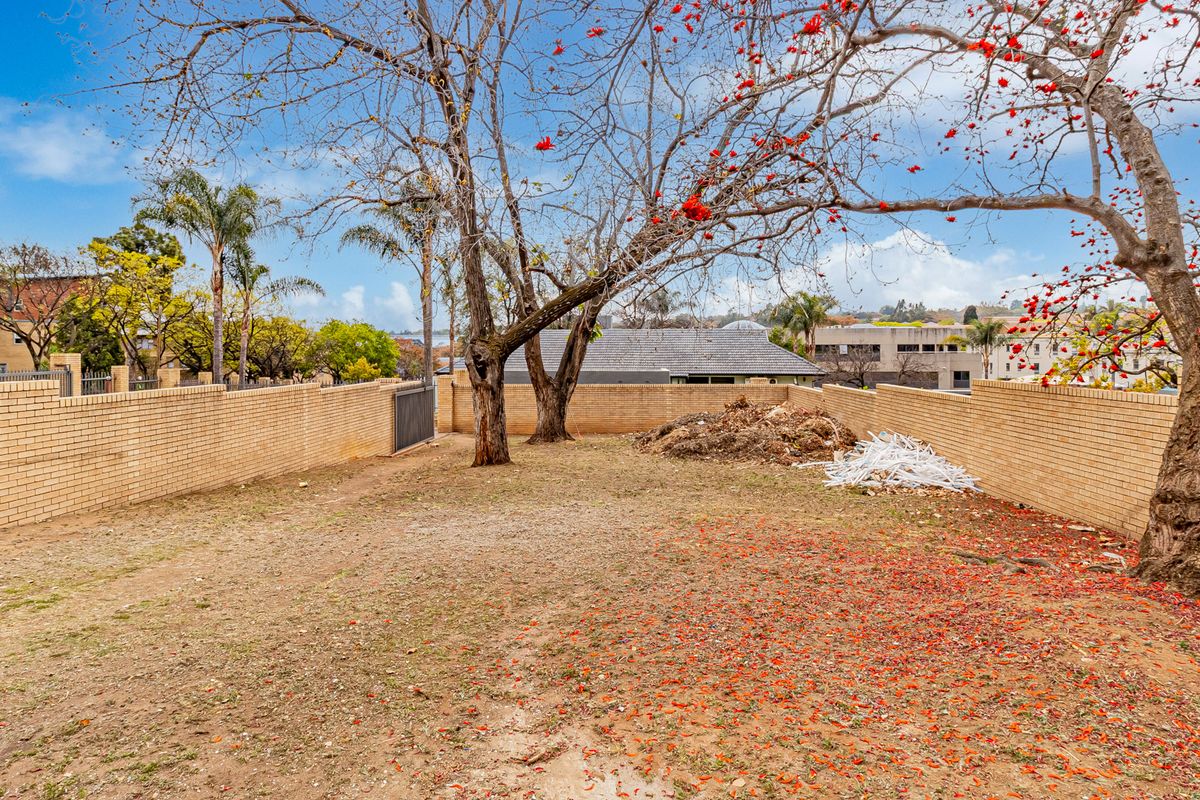 A spacious rear outdoor area enclosed by brick boundary walls, featuring mature trees and requiring landscaping and debris removal.