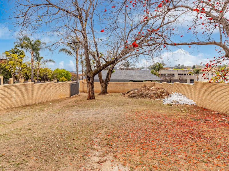 A spacious rear outdoor area enclosed by brick boundary walls, featuring mature trees and requiring landscaping and debris removal.