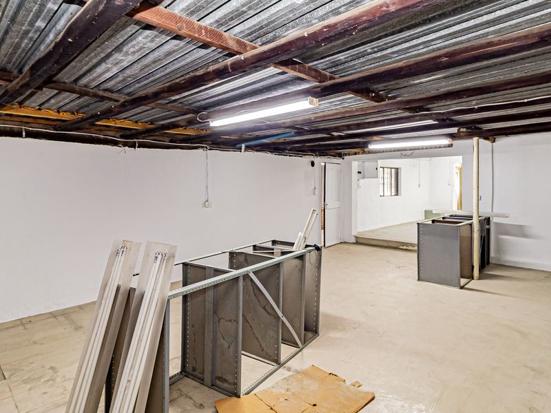 An open-plan office space featuring an industrial-style exposed corrugated metal ceiling, fluorescent lighting, and concrete flooring, currently in a shell-like condition.