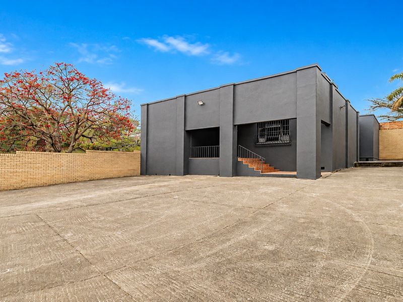 Rear exterior view of the office building featuring a large concrete parking area, brick boundary walls, and secure access points.