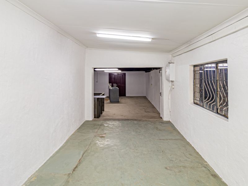 A functional utility or storage space featuring painted concrete flooring, security bars on the window, and overhead fluorescent lighting.