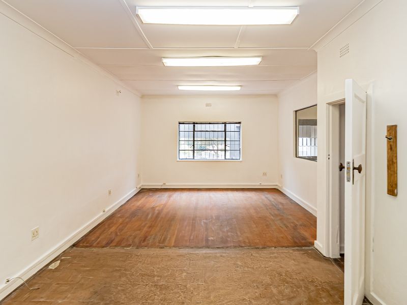 A vacant office space featuring timber flooring, fluorescent lighting, and security bars on the windows, offering a blank canvas for professional use.