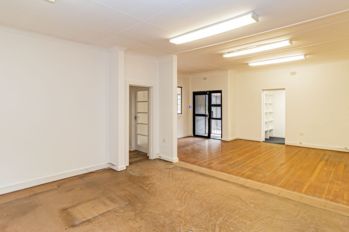 Spacious open-plan office area featuring hardwood flooring, bright fluorescent lighting, and built-in shelving, offering a versatile workspace layout.