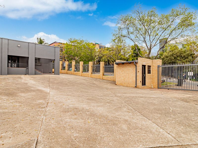 Front exterior view of the office property featuring a concrete driveway, security guard house, and perimeter fencing.
