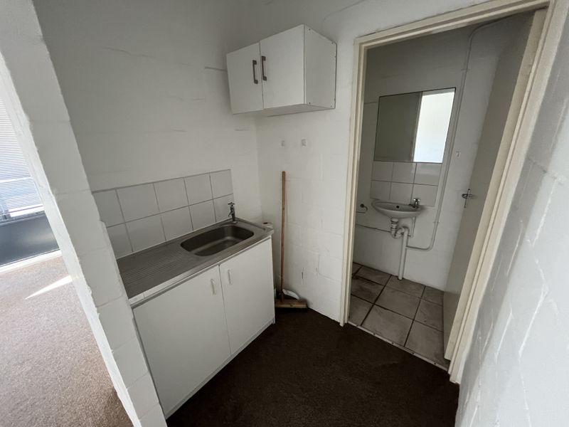A functional utility area featuring a stainless steel sink, built-in cabinetry, and an adjoining small washroom with a wall-mounted basin.