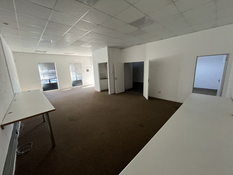 Open plan office space featuring a suspended ceiling, carpeted flooring, and a small built-in kitchenette area.