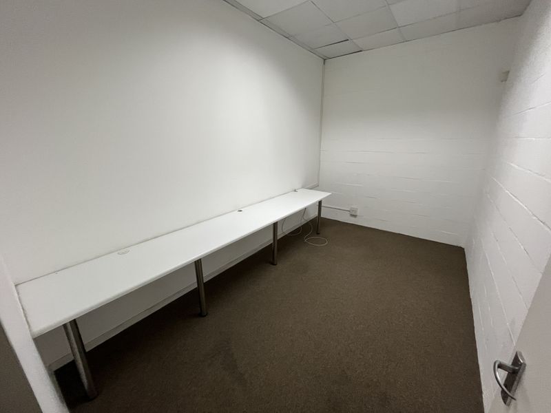 A functional office space featuring a long built-in desk, carpeted flooring, and a suspended ceiling, suitable for a professional workspace.