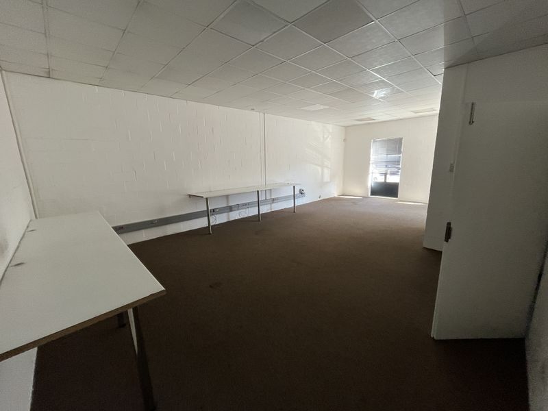 An open-plan industrial office space featuring suspended ceilings, carpeted flooring, and functional wall-mounted electrical trunking, offering a blank canvas for business operations.