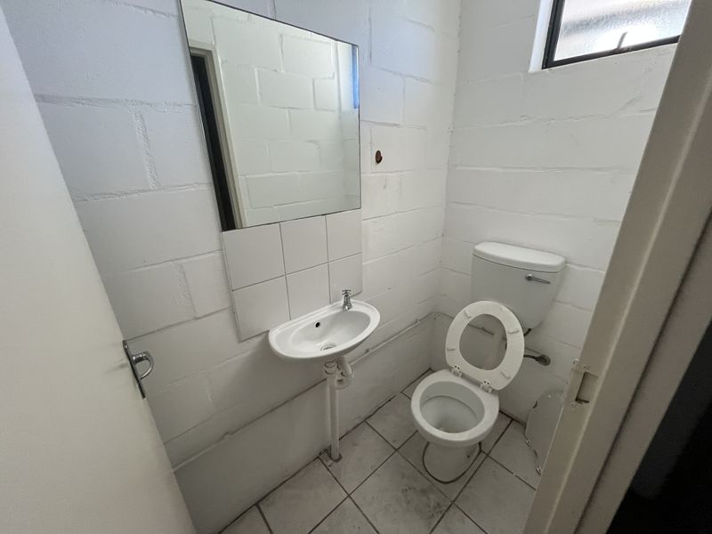 A compact industrial-style bathroom featuring a wall-mounted basin, toilet, and tiled flooring with exposed blockwork walls.