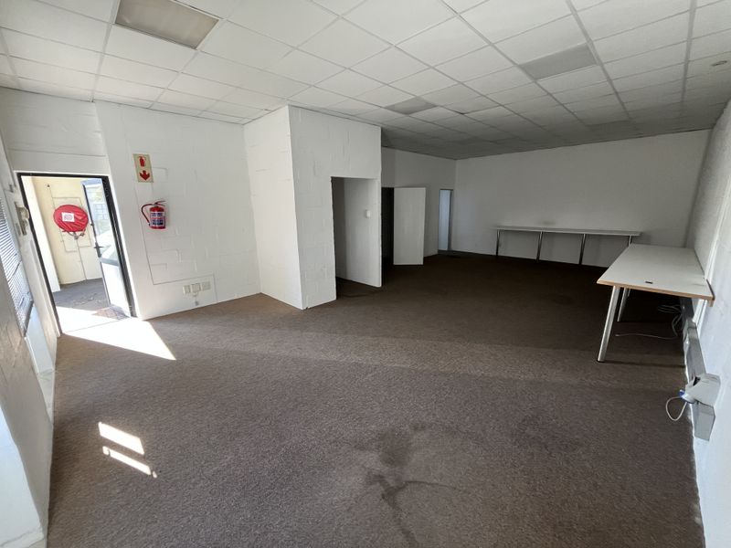 An open-plan industrial office space featuring a suspended ceiling, carpeted flooring, and integrated fire safety equipment.