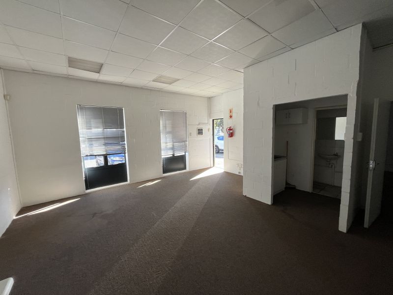 Open plan industrial office space featuring a suspended ceiling, carpeted flooring, integrated kitchenette, and a private bathroom facility.