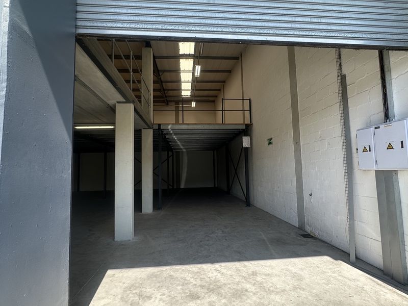 Spacious industrial warehouse unit featuring a high-clearance roller shutter door, concrete flooring, and a functional mezzanine level for additional storage or office space.