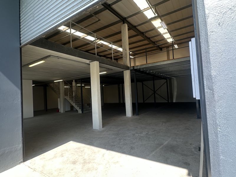 Spacious industrial warehouse unit featuring a large roller shutter door, concrete flooring, and a functional mezzanine level with integrated staircase and overhead lighting.