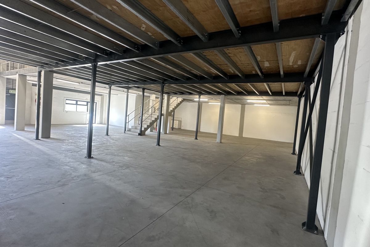 Spacious industrial open-plan warehouse area featuring a steel mezzanine level, concrete flooring, and a functional staircase, suitable for various commercial or storage uses.