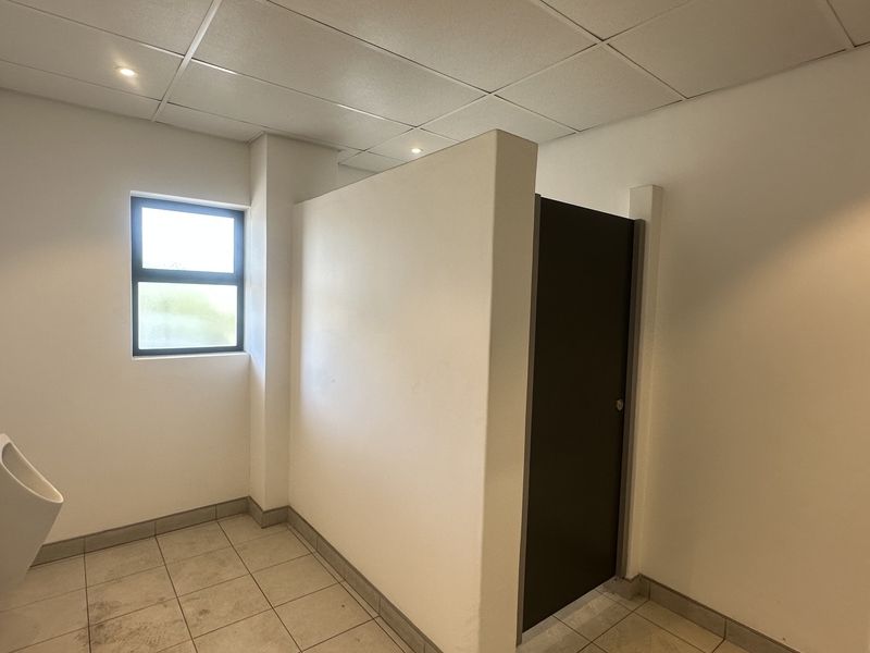 A functional industrial restroom facility featuring tiled flooring, a wall-mounted urinal, and a private partitioned stall.