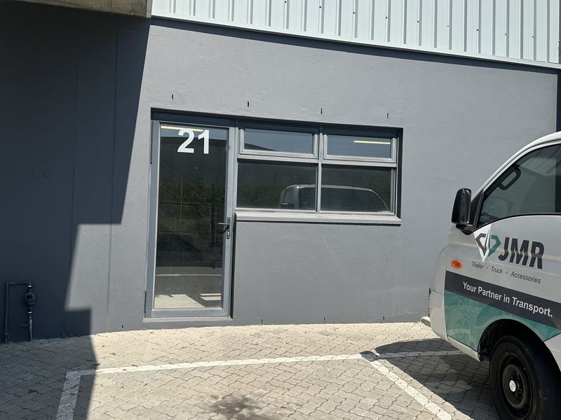 Front entrance of an industrial unit featuring a glass door and window, finished with a modern grey facade and paved parking area.