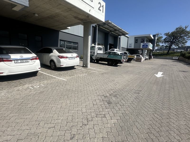 Front exterior view of an industrial property featuring a paved parking area, concrete canopy, and multiple roller shutter access doors.