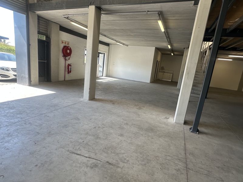 Spacious industrial warehouse unit featuring concrete flooring, a mezzanine level, roller shutter access, and integrated fire safety equipment.