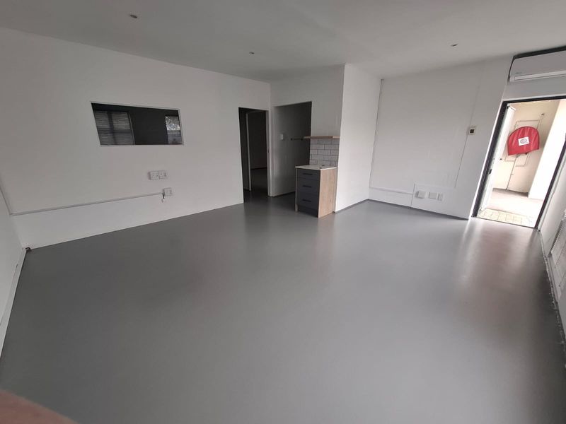 A clean, open-plan industrial space featuring smooth epoxy flooring, recessed lighting, a wall-mounted air conditioner, and a compact kitchenette area.