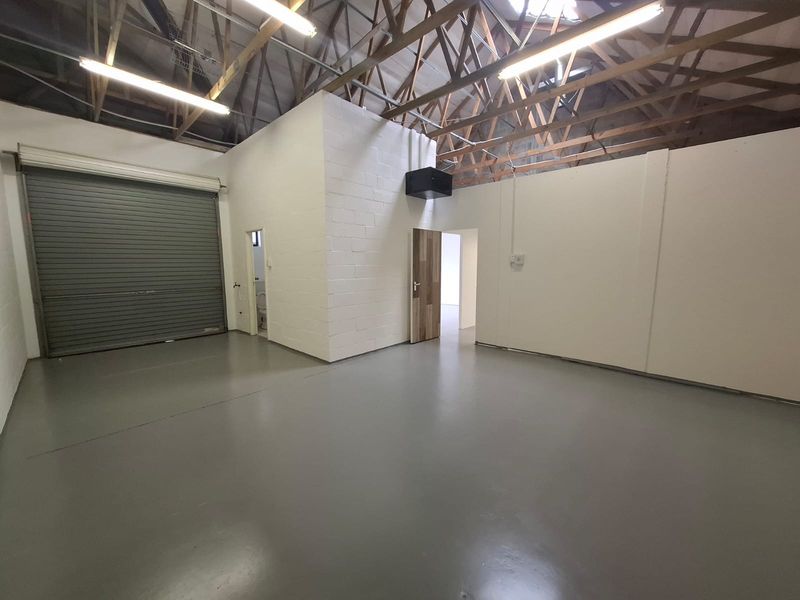 Spacious industrial garage featuring high ceilings with exposed timber trusses, durable epoxy flooring, and a large roller shutter door for easy access.