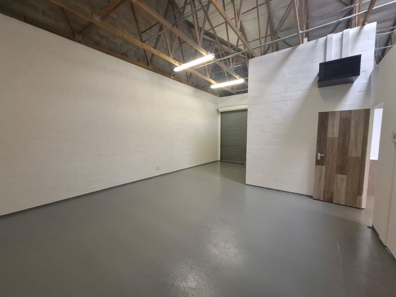 A clean, open-plan industrial utility space featuring exposed timber roof trusses, durable epoxy flooring, and a secure roller shutter door.