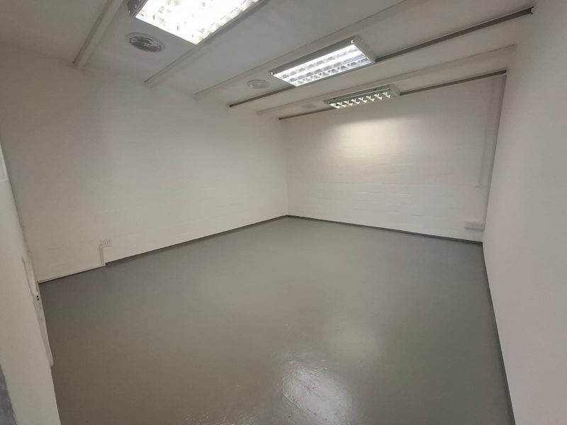 A clean, empty industrial office space featuring durable epoxy flooring, painted brick walls, and overhead fluorescent lighting.