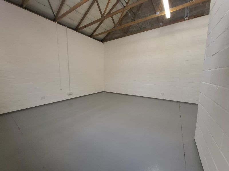 A clean, empty industrial utility space featuring exposed timber roof trusses, painted block walls, and a durable epoxy-coated concrete floor.