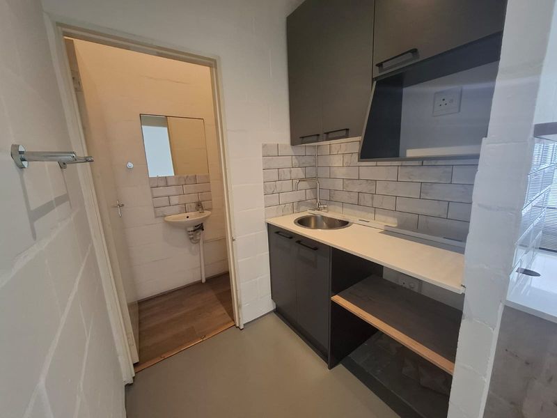 A compact scullery area featuring modern dark cabinetry, a stainless steel sink, subway tile backsplash, and an adjacent small washroom with a basin.