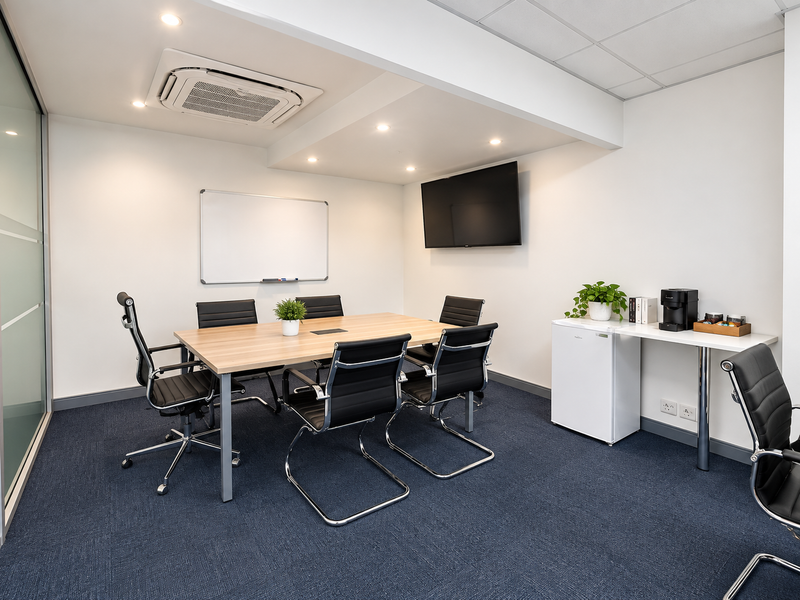 A professional meeting room featuring recessed lighting, integrated air conditioning, wall-mounted media facilities, and durable carpet flooring.