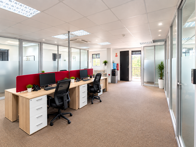 A modern, well-lit office space featuring glass partitions, carpeted flooring, and a suspended ceiling, providing a professional and functional work environment.
