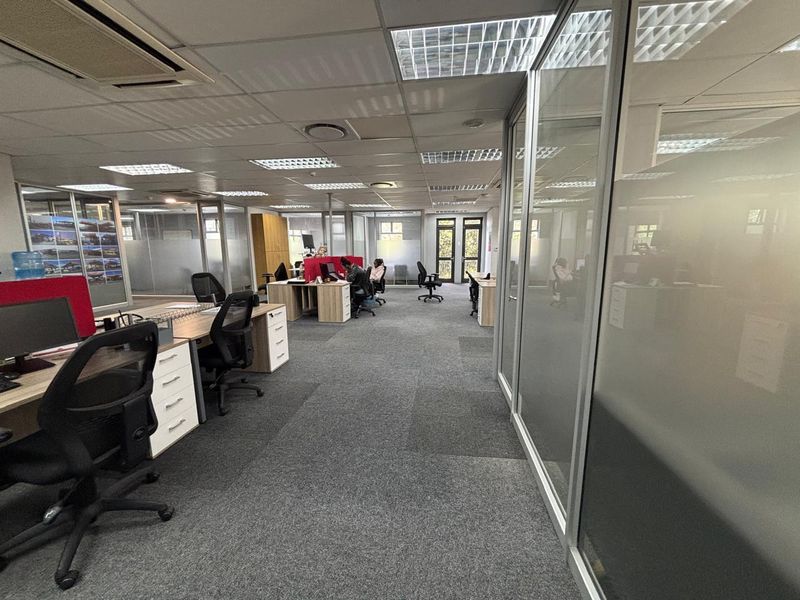 Open plan office space featuring glass partitioning, suspended ceilings with recessed lighting, and carpeted flooring.