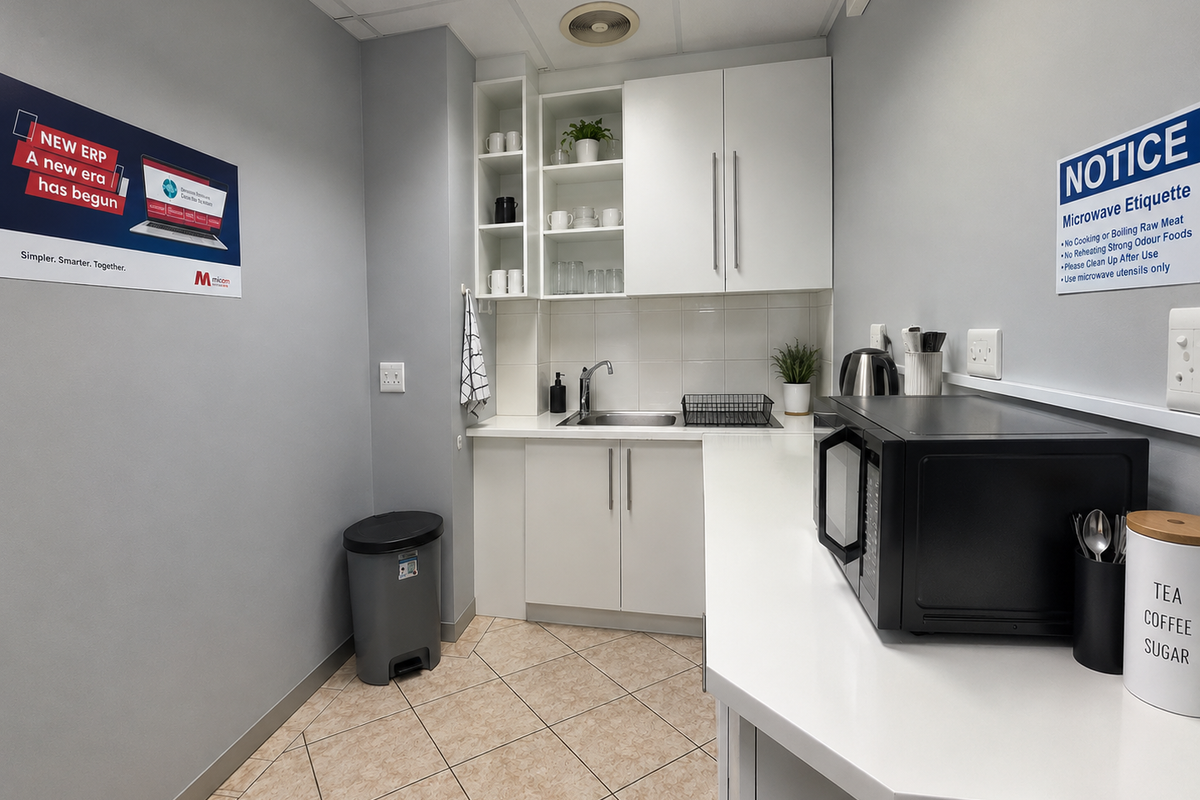 A functional office kitchenette featuring white cabinetry, a stainless steel sink, tiled backsplash, and ample counter space for staff use.