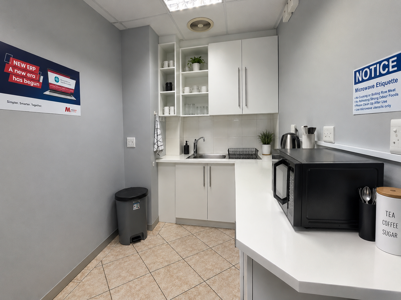A functional office kitchenette featuring white cabinetry, a stainless steel sink, tiled backsplash, and ample counter space for staff use.