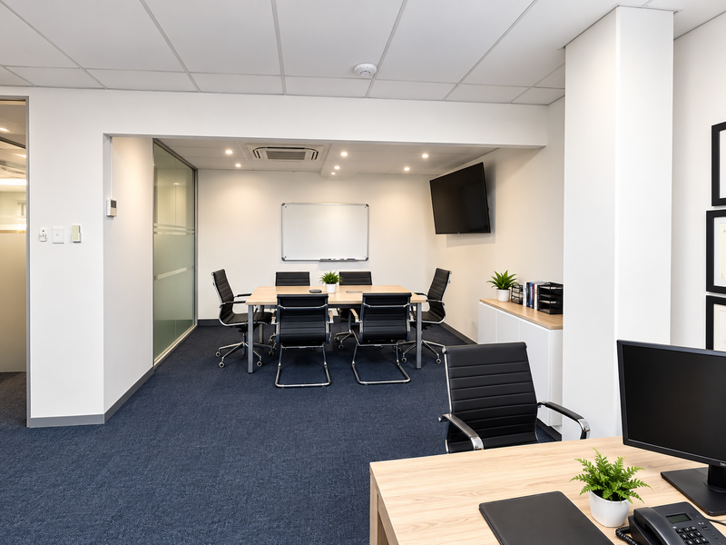 A professional office space featuring a meeting area with a whiteboard, suspended ceiling with recessed lighting, and modern glass partitioning.