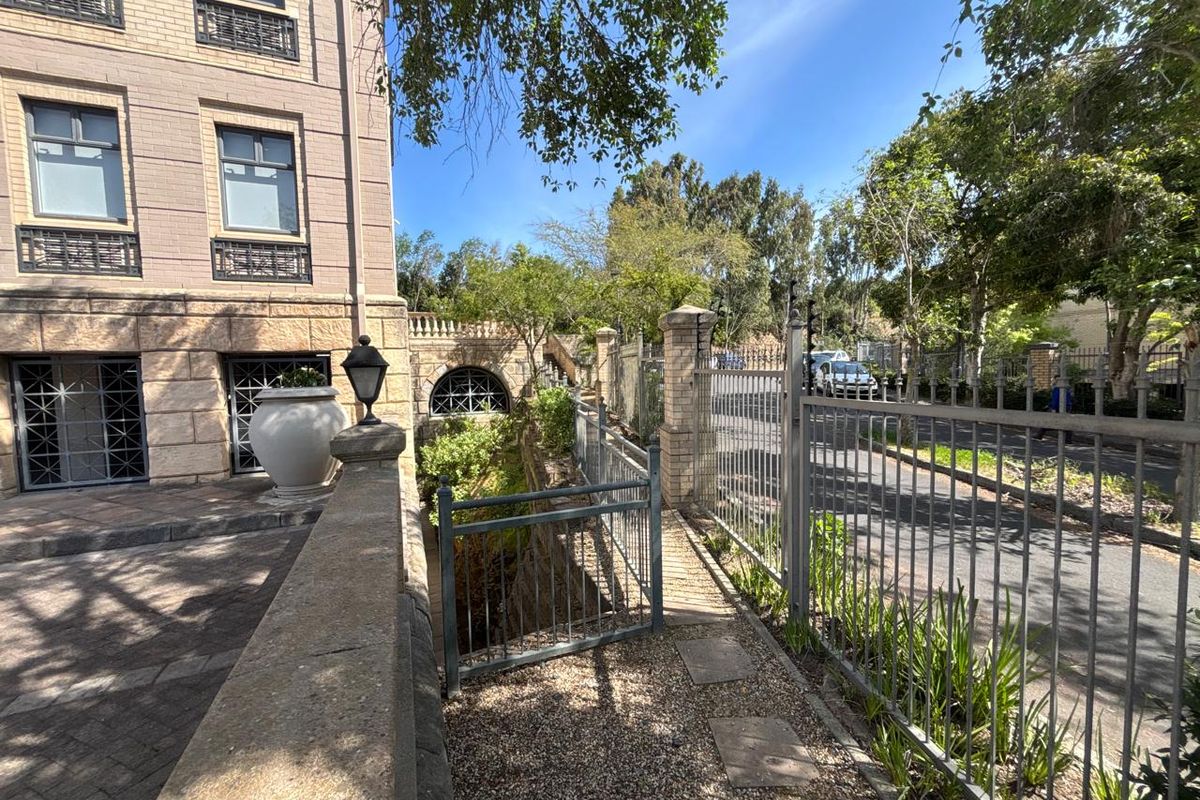 A well-maintained exterior rear area featuring stone masonry, metal security fencing, and a paved walkway alongside the office building structure.
