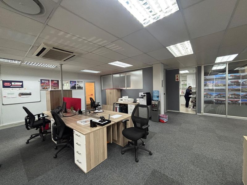 A functional open-plan office space featuring suspended ceilings, recessed lighting, ducted air conditioning, carpeted flooring, and an integrated kitchenette area.