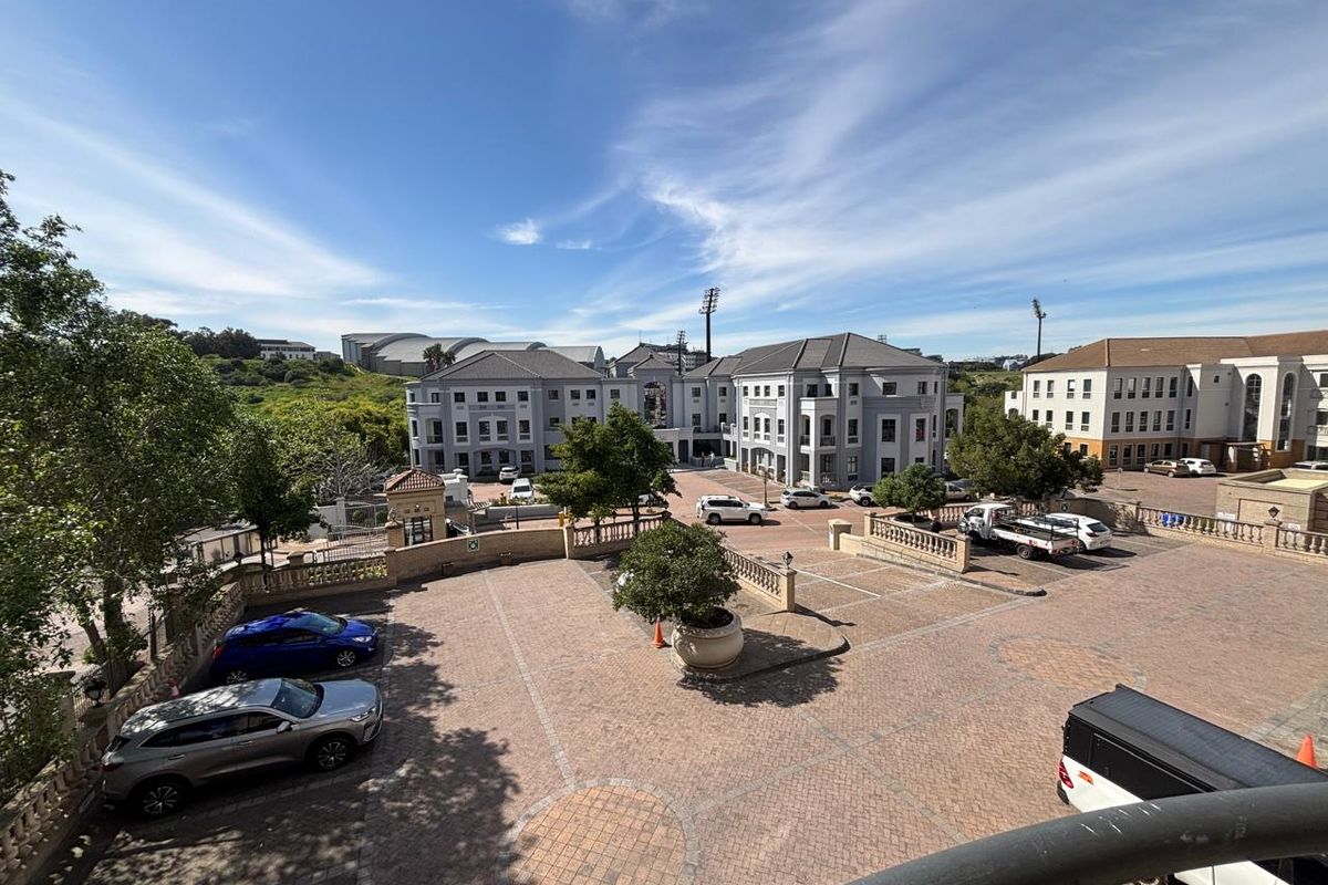 Elevated view overlooking a paved office complex courtyard with surrounding multi-story commercial buildings and landscaped grounds.