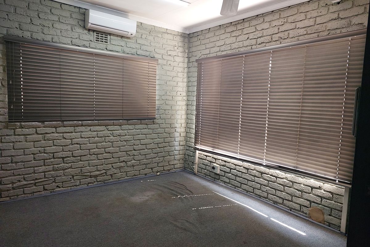 A vacant office space featuring exposed brick walls, carpeted flooring, split-system air conditioning, and venetian blinds.