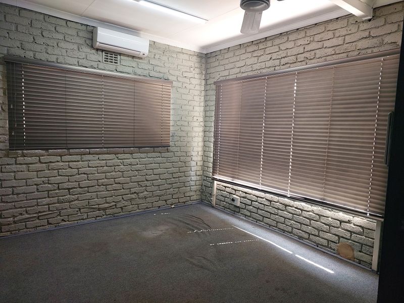 A vacant office space featuring exposed brick walls, carpeted flooring, split-system air conditioning, and venetian blinds.