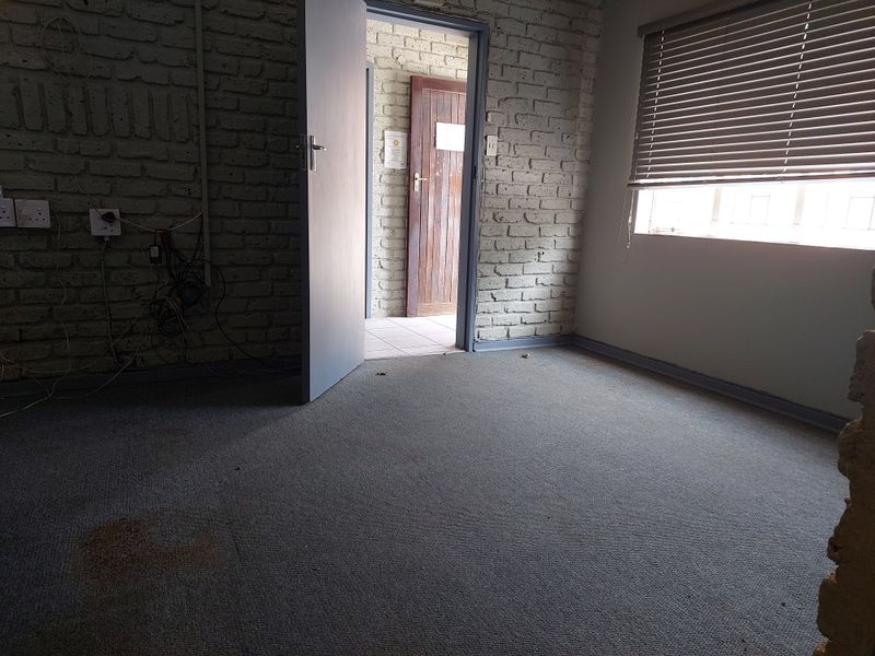 An empty office space featuring exposed brick walls, carpeted flooring, and venetian blinds, providing a blank canvas for professional workspace customization.