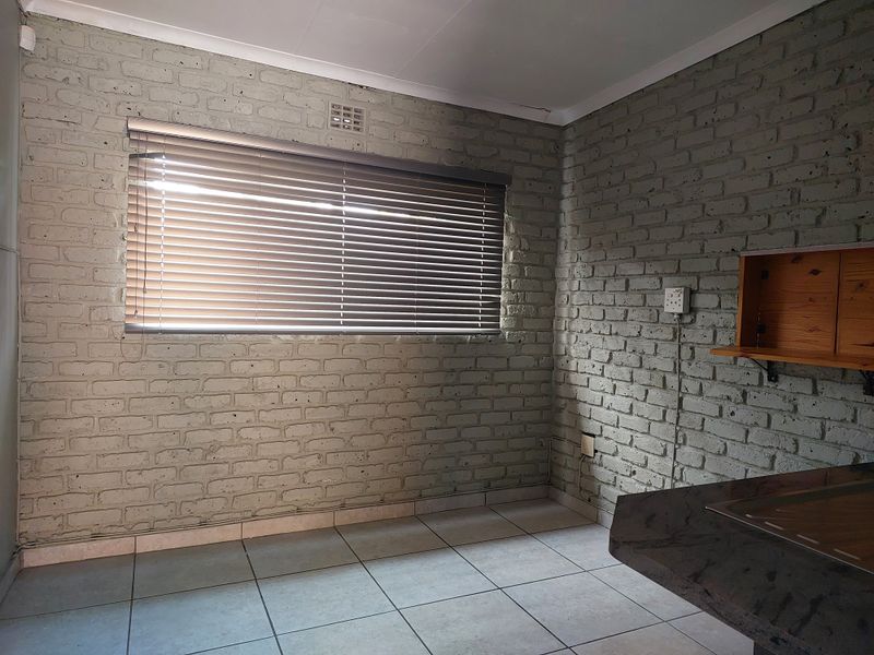 An empty office space featuring painted brick walls, ceramic tiled flooring, and built-in shelving, providing a functional and neutral workspace environment.