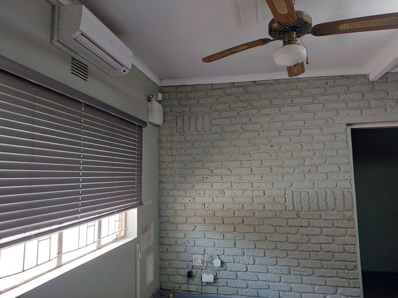 An office space featuring an exposed brick wall, split-system air conditioning, a ceiling fan, and venetian blinds.
