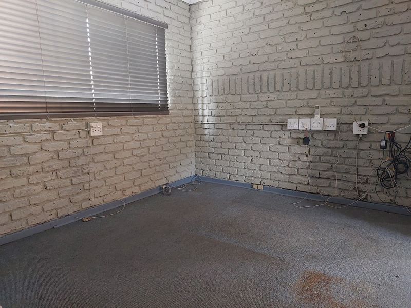 Empty office space featuring exposed brick walls, carpeted flooring, and multiple electrical power points with surface-mounted wiring.