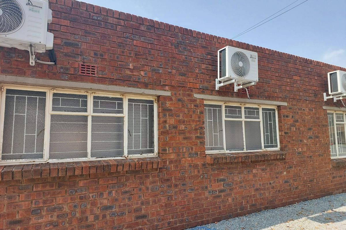 Exterior view of a face brick office building featuring multiple wall-mounted air conditioning units and steel-framed windows with security bars.