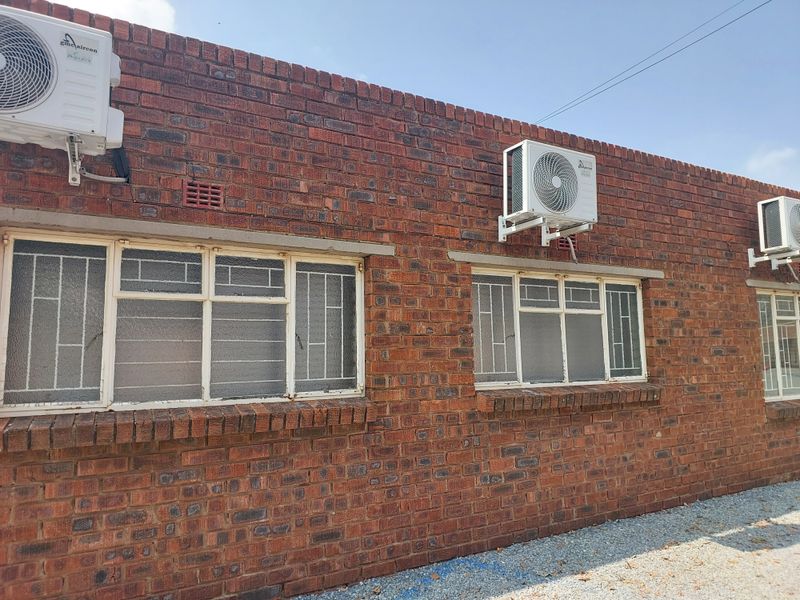 Exterior view of a face brick office building featuring multiple wall-mounted air conditioning units and steel-framed windows with security bars.