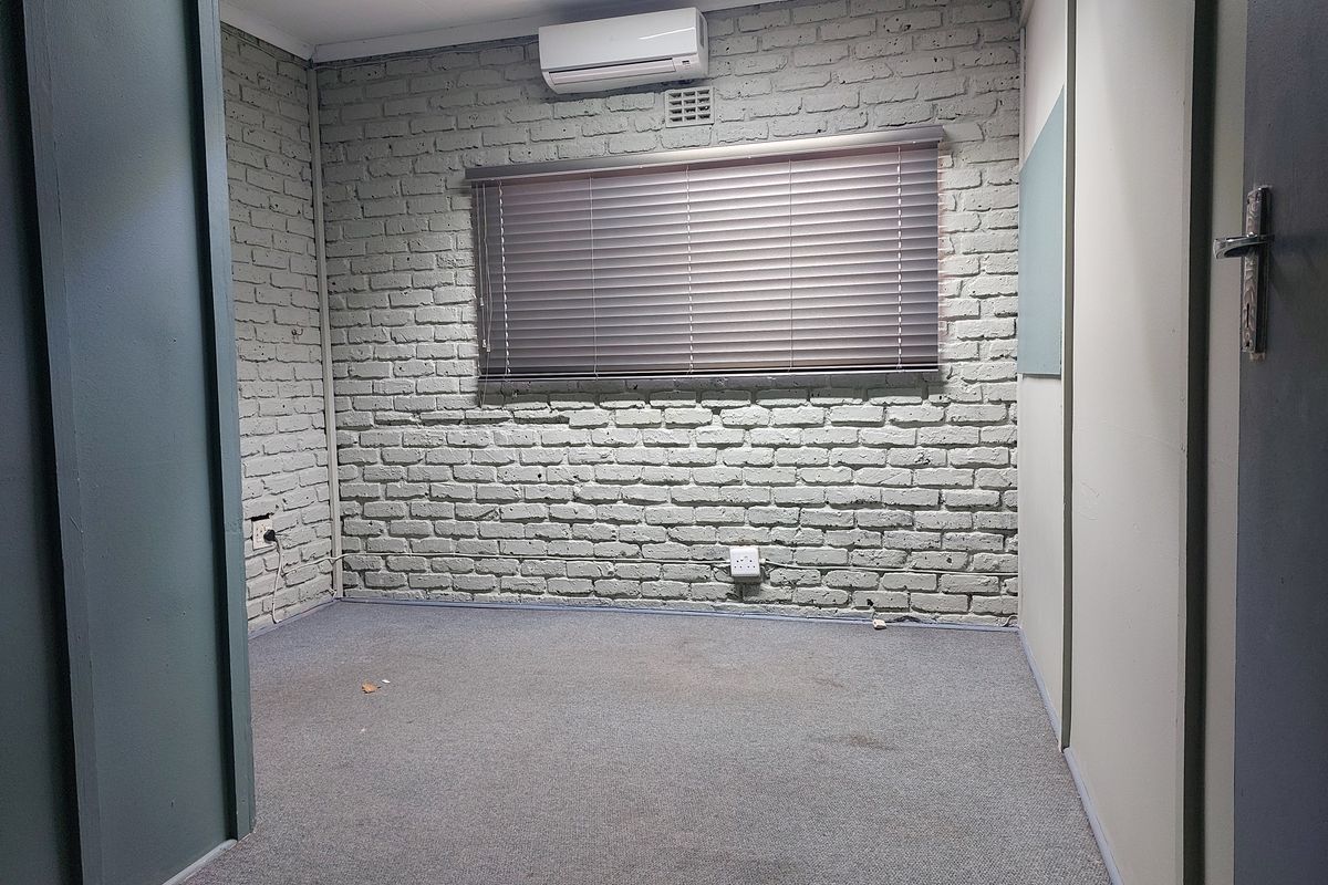 A vacant office space featuring a painted brick feature wall, split-system air conditioning, and carpeted flooring.