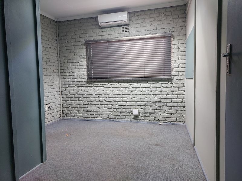 A vacant office space featuring a painted brick feature wall, split-system air conditioning, and carpeted flooring.