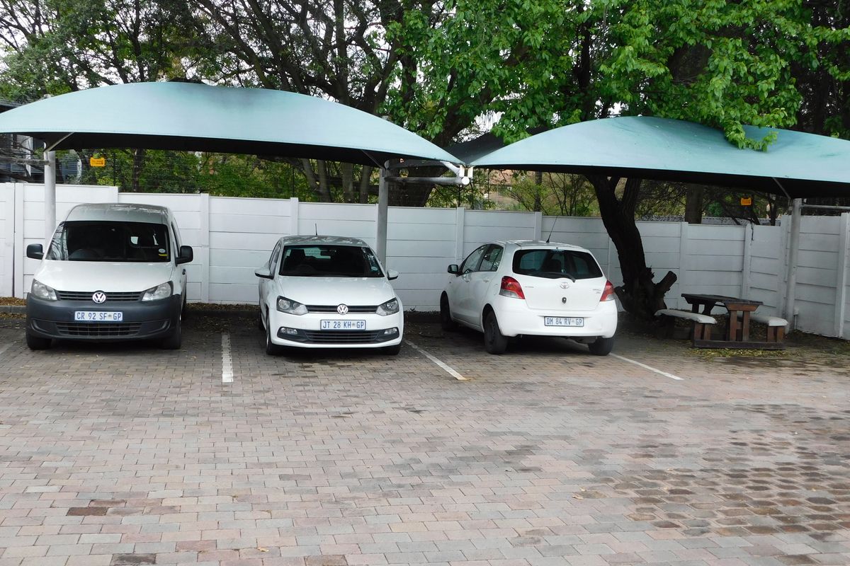Outdoor parking area featuring paved bays covered by shade cloth structures and enclosed by a precast concrete boundary wall.