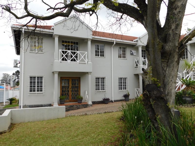A well-maintained two-story office building featuring a classic facade, terracotta roof tiles, balconies, and secure window treatments set within a landscaped garden.
